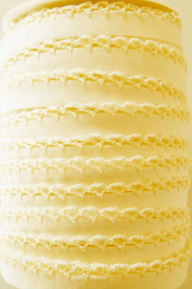 Puede incluir: Un rollo de ribete de crochet blanco marfil con un borde festoneado. El ribete est&aacute; hecho de un material suave y delicado y tiene un brillo sutil.