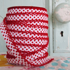May include: A spool of red and white polka dot ribbon with a red crocheted trim. The ribbon is wound around a cardboard spool.