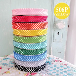 May include: A stack of ten polka dot fabric ribbon rolls in various colors, including pink, red, orange, yellow, green, blue, gray, and black. The ribbon rolls are stacked on a floral patterned surface. The text "506P YELLOW" is visible in a yellow circle.