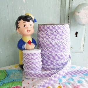 May include: Two spools of lavender gingham ribbon with white lace trim. The ribbon is wound around the spools and is ready to be used for crafting or decorating.