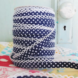 Peut inclure: Un rouleau de ruban bleu marine à pois blancs et une bordure en dentelle blanche. Le ruban est enroulé serré, mettant en valeur le motif et la texture. La bordure en dentelle ajoute une touche délicate.