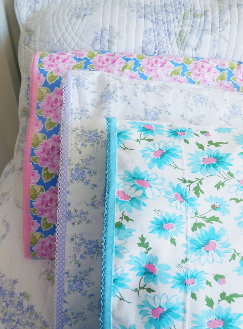 Peut inclure: Quatre taies d'oreiller avec des motifs floraux. La taie d'oreiller du haut a un motif floral rose et bleu. La deuxi&egrave;me taie d'oreiller a un motif floral bleu clair. La troisi&egrave;me taie d'oreiller a un fond blanc avec un motif floral bleu et rose. La taie d'oreiller du bas a un fond blanc avec un motif floral bleu.