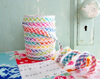 Könnte beinhalten: Eine Rolle buntes Gingham-Band mit weißer Spitzenborte. Das Band ist in den Farben Rosa, Blau, Grün und Gelb gehalten. Das Band liegt auf einem Tisch mit einem handgeschriebenen Zettel, auf dem "Victorian free tage for me home love, new" steht.