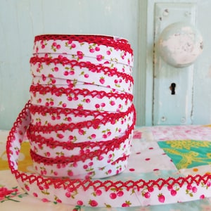 Peut inclure: Un rouleau de galon en tissu blanc avec un bord en crochet rouge et un petit imprim&eacute; de cerises rouges.