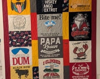 Può includere: Una trapunta colorata realizzata con t-shirt riutilizzate. La trapunta presenta una varietà di disegni e testi, tra cui "Whiskey Tango Foxtrot", "Bite me!", "Grandpa", "Grumpy", "Tweedle Dum", "Papa Knows", "I Climbed" e "Up in Smoke Firewood".
