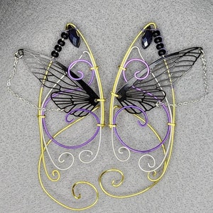 May include: A pair of black and white butterfly wings made of wire, with purple and gold accents. The wings are attached to a chain and have black beads hanging from them.