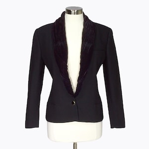 May include: A black blazer with a dark velvet collar. The jacket features a single gold button and two front pockets. The garment is displayed on a mannequin.