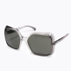 Peut inclure: Une paire de lunettes de soleil surdimensionnées transparentes avec des verres gris foncé. Les lunettes ont une forme carrée aux coins arrondis.