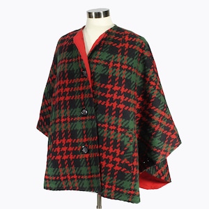 May include: A red, green, and black plaid cape with a red lining and three black buttons. The cape has a short, wide shape and is made of a thick, woven fabric.