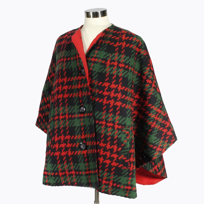 May include: A red, green, and black plaid cape with a red lining and three black buttons. The cape has a short, wide shape and is made of a thick, woven fabric.