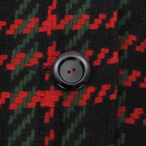 May include: A close-up of a black button with a red thread loop on a red and green plaid fabric.