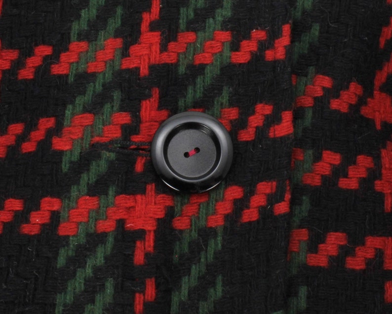 May include: A close-up of a black button with a red thread loop on a red and green plaid fabric.