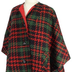 May include: A red and green plaid wool poncho with a black background. The poncho has a red lining and three black buttons down the front.