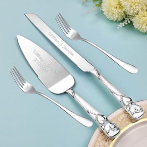 May include: A silver wedding cake knife and server set with a silver fork. The knife and server have a heart-shaped design with rhinestones. The handles are engraved with the names "William & Jennifer" and the date "08.18.2023". The fork is engraved with "Mr & Mrs".
