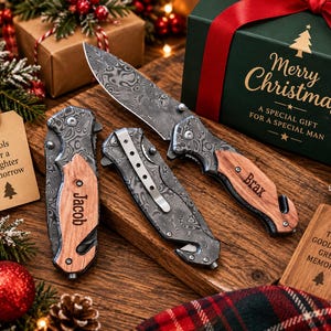May include: Two folding pocket knives with Damascus steel blades and wooden handles. One knife is open, showing the patterned blade, while the other is closed, displaying a metal pocket clip. The handles are engraved with the names Jacob and Brax.