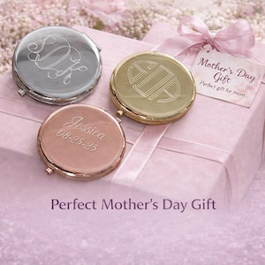 May include: Three personalized compact mirrors in silver, gold, and rose gold, each with unique engraved designs. The mirrors rest on a pink gift box tied with a ribbon, with a tag that reads "Mother's Day Gift". The image is set against a backdrop of pink flowers.