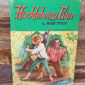 May include: A green book cover with the title "Huckleberry Finn" by Mark Twain. The cover features an illustration of two boys fishing on a raft.