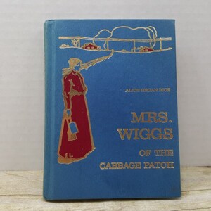 May include: A blue book cover with gold lettering. The title is "Mrs. Wiggs of the Cabbage Patch" by Alice Hegan Rice. The cover features a woman in a red dress holding a bucket.