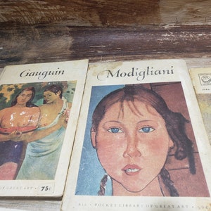 May include: Three vintage paperback books about famous artists. The book on the left features a painting of two women, one holding a watermelon. The middle book features a portrait of a young woman with blue eyes. The book on the right has the title "Klee" and the name "Jurg Spiller" printed on the cover.