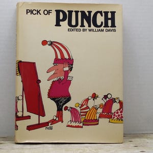May include: A vintage book cover with the title "Pick of Punch" and the text "Edited by William Davis". The cover features a cartoon illustration of a man in a red and white striped hat looking at himself in a mirror. There are several other hats in the background.