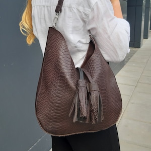 May include: A brown leather handbag with a snakeskin pattern and a tassel detail.