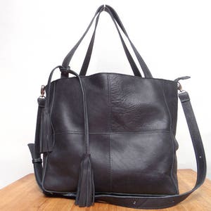 Peut inclure: Un sac cabas en cuir noir avec deux longues lanières et deux accents en pompon. Le sac a une forme structurée et un design en patchwork.