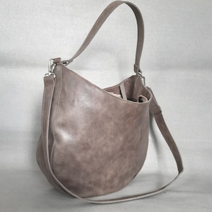 Könnte beinhalten: Eine braune Ledertasche im Hobo-Stil mit einem langen Riemen. Die Tasche hat eine geschwungene Form und eine glatte, strukturierte Oberfläche.