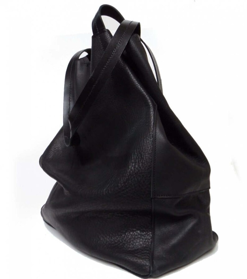 May include: A large, black leather tote bag with a slouchy, unstructured design. The bag has two long straps and a wide opening.