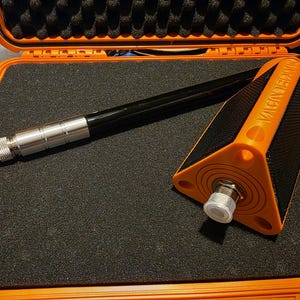 May include: An orange and black triangular tool with the text VACUUMEDDIY printed on the side, featuring a silver metallic connector and a long black rod, all resting inside an orange protective case with black foam padding.