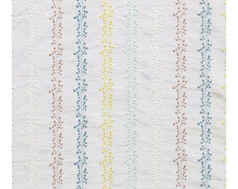 Puede incluir: Tela blanca con rayas verticales de color rosa, azul, amarillo y azul claro. Cada raya presenta un patrón repetitivo de pequeños puntos bordados.