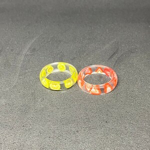 May include: Two clear resin rings with embedded fruit slices. One ring has yellow lemon slices and the other has red strawberry slices.