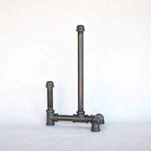 May include: A black metal pipe towel rack with a vertical pipe and a horizontal pipe extending to the side. The rack has four black metal pipe feet.