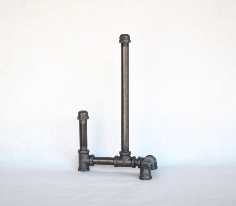 May include: A black metal pipe towel rack with a vertical pipe and a horizontal pipe extending to the side. The rack has four black metal pipe feet.