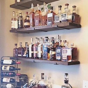 May include: A home bar setup featuring two dark wooden shelves filled with various liquor bottles. A wine rack with several bottles is visible below. The bottles are of different shapes and sizes, with a variety of labels.