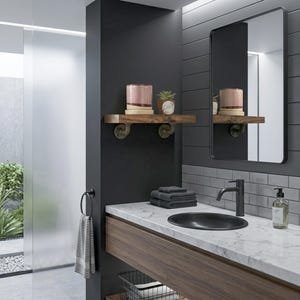 May include: A bathroom vanity featuring a white marble countertop with a black oval sink and a black faucet. Above, a wooden shelf with metal pipe brackets holds a pink candle and a small succulent. A rectangular mirror hangs on the wall.