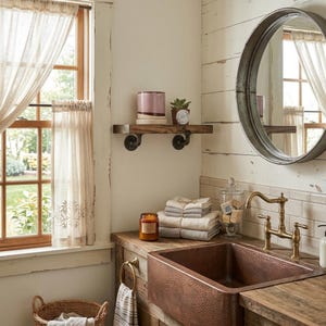 May include: A bathroom vanity area featuring a hammered copper farmhouse sink, a brass faucet, and a wooden countertop. Above, a round metal-framed mirror hangs near a floating wooden shelf with a pink ceramic cup and a small potted succulent.