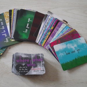 May include: A deck of Future Love Oracle Cards with a purple heart and the text "where what who" on the front. The cards are spread out on a wooden surface. One card is face up and shows a blue sky with white clouds and the text "lives near you".