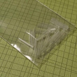 May include: A clear plastic bag containing a collection of small, transparent plastic tubes. The tubes are cylindrical and appear to be hollow. The bag is resting on a green, textured surface.