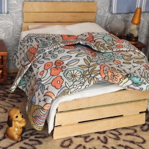 May include: Miniature wooden bed with a floral patterned comforter in orange, blue, and green. A small brown dog figurine sits on the patterned rug in front of the bed. The bed is made of light-colored wood.