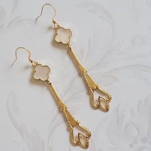 Peut inclure: Une paire de boucles d'oreilles en or avec une pierre blanche en forme de trèfle et un motif en filigrane doré.