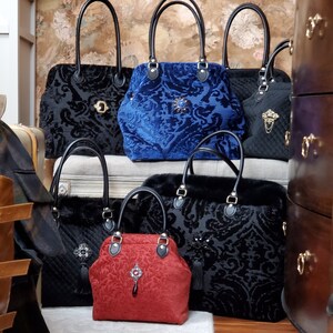 Collection of handcrafted carpet bags created with upholstery fabric in blacks, red and blue. Each features black leather handles and a vintage brooch accent.