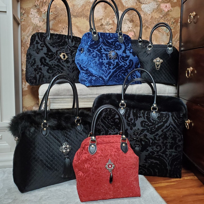 Collection of handcrafted carpet bags created with upholstery fabric in blacks, red and blue. Each features black leather handles and a vintage brooch accent.