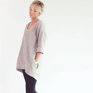 May include: A woman wearing a gray oversized sweater, black leggings, and black rain boots.