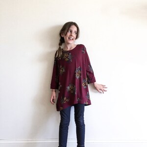 May include: A young person wearing a maroon floral print long-sleeved shirt and blue jeans.