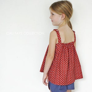 May include: A young girl wearing a red sleeveless top with a white floral pattern and blue denim shorts. The top has a gathered neckline and thin straps. The text "CALI FAYE COLLECTION." is visible in the background.