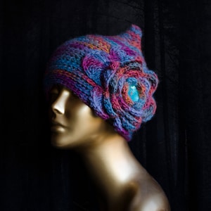 May include: A purple, blue and orange crocheted hat with a large crocheted flower on the side. The flower has a turquoise gem in the centre.