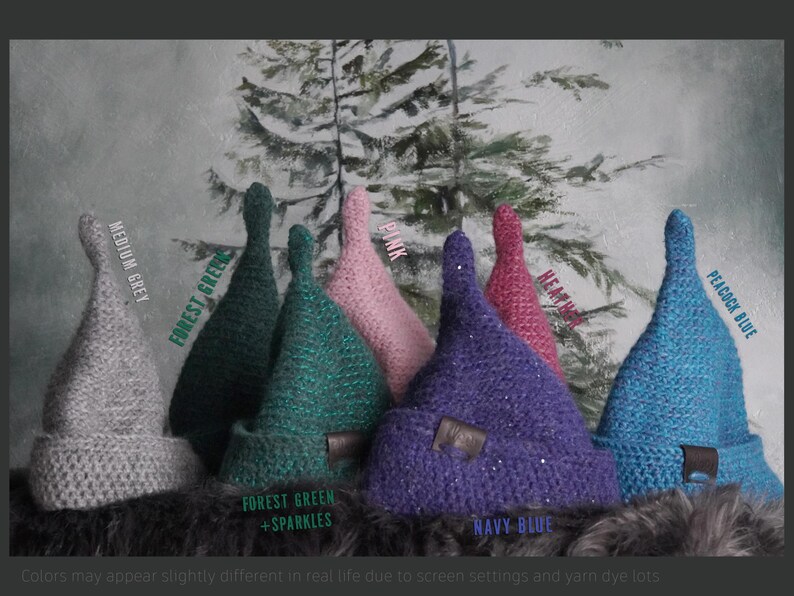 Op de afbeelding: Een collectie van zeven gehaakte puntmutsen in diverse kleuren, waaronder middengrijs, bosgroen, bosgroen met glitters, roze, paars, heidekleur en pauwblauw. Elke muts is voorzien van een omgeslagen rand en een klein bruin leren label.