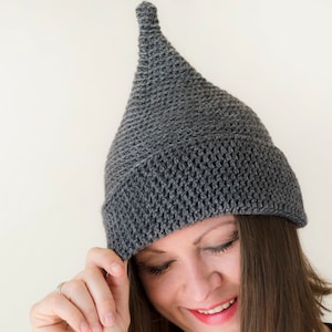Può includere: Un cappello di lana grigio con la cima a punta. Il cappello è tirato giù sulla fronte della persona, e lei sorride.
