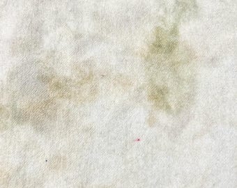 May include: A textured fabric surface featuring an off-white base color with soft, blended patches of muted olive green and light tan. The material displays a woven, fibrous appearance with a single tiny red dot and a small blue speck.