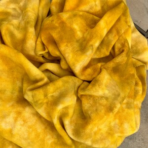 May include: A yellow fabric with a tie-dye pattern. The fabric is folded and crumpled, showing the texture and color variations.